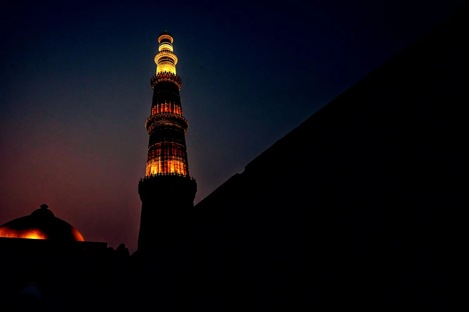 The Qutub Minar at blue hour, its silhouette rising against a deep indigo sky