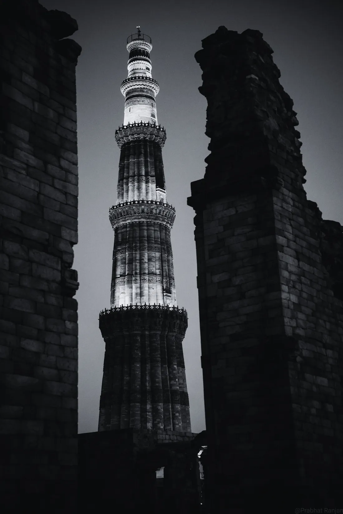 The Qutub Minar lit in warm gold at night, framed by dark stone